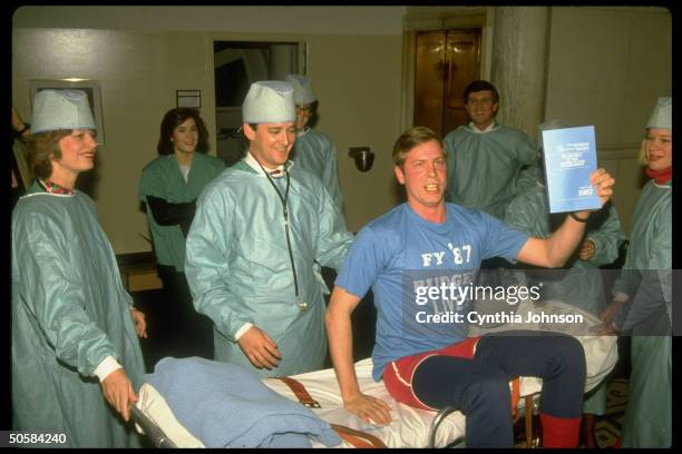 Office of Management and Budget jokesters staging surgical delivery of fiscal yr. 1987's budget, w. Man in t-shirt as living patient .