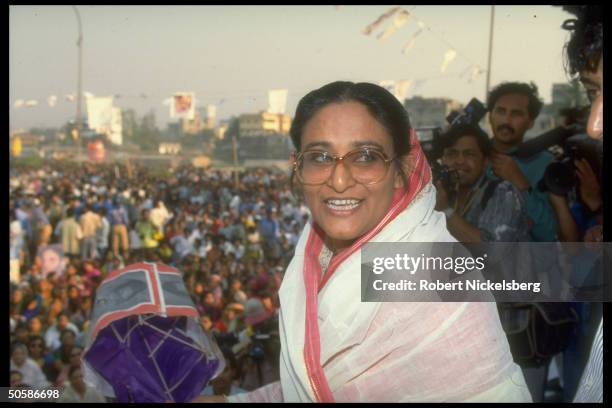 Awami League ldr. Sheik Hasina Wazed on stump, holding party campaign item, during crowded election campaign rally.