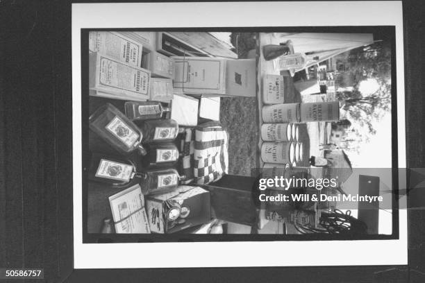 Cans of sardines, sliced bacon, army beans, potted Possum sauce and beef stew sitting on makeshift shelves along w. Bottles of whisky and medication...