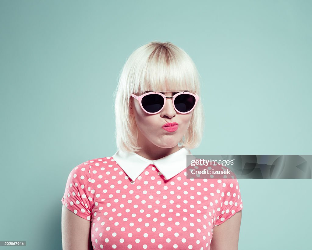 Cute blonde young woman wearing polka dotted dress making faces