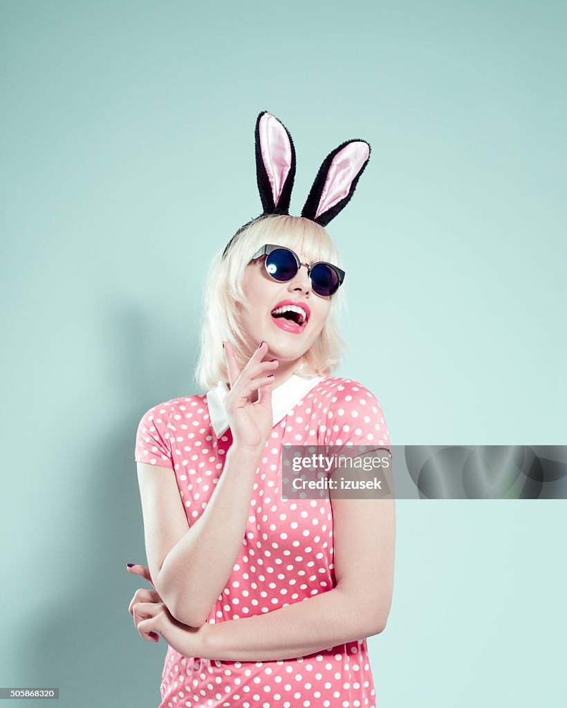 Excited blonde young woman wearing rabbit ears headband and sunglasses