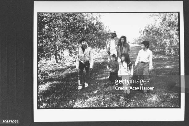 Mexican Migrant farmer Manuel Ortiz w. Arm around wife Rosa Maria walking through apple orchard w. Their 4 kids.