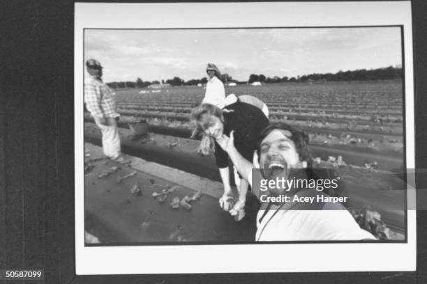 Mexican & American Migrant farmers planting strawberries in field w. Photographer Acey Harper smiling in foreground.