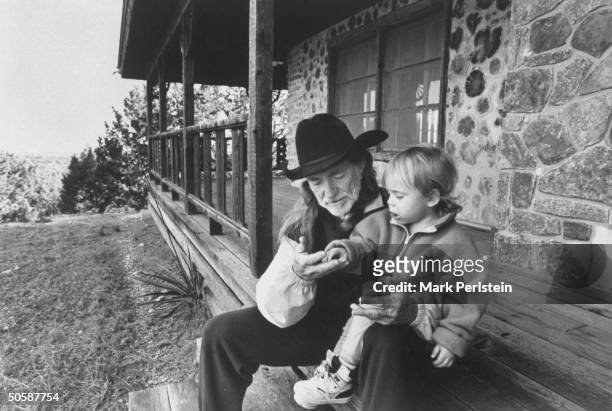 Singer Willie Nelson w. His son Lukas Autry chatting as they sit on front steps of his barren cabin which the IRS stripped of its furniture after it...