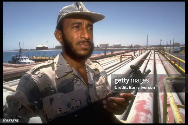 Armed security guard poised by pipelines & port facilties at Saudi Aramco oil refinery & loading terminal at Ras Tanura, Saudi Arabia.