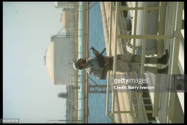 Armed security guard poised by pipelines & port facilties at Saudi Aramco oil refinery & loading terminal at Ras Tanura, Saudi Arabia.