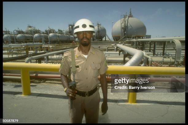 Armed security guard poised by pipelines & storage tanks at Saudi Aramco oil refinery & loading terminal at Ras Tanura, Saudi Arabia.