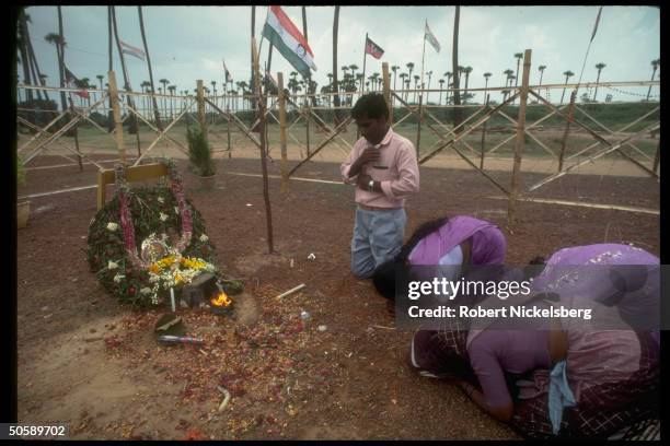 Locals bowing, prayer-like, at wreath-adorned site of bombing that killed ex-PM Rajiv Gandhi during election campaign halted by his assassination.