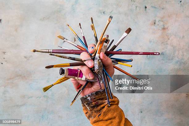 hand holding cluster of paint brushes and paints - kunstenaar stockfoto's en -beelden