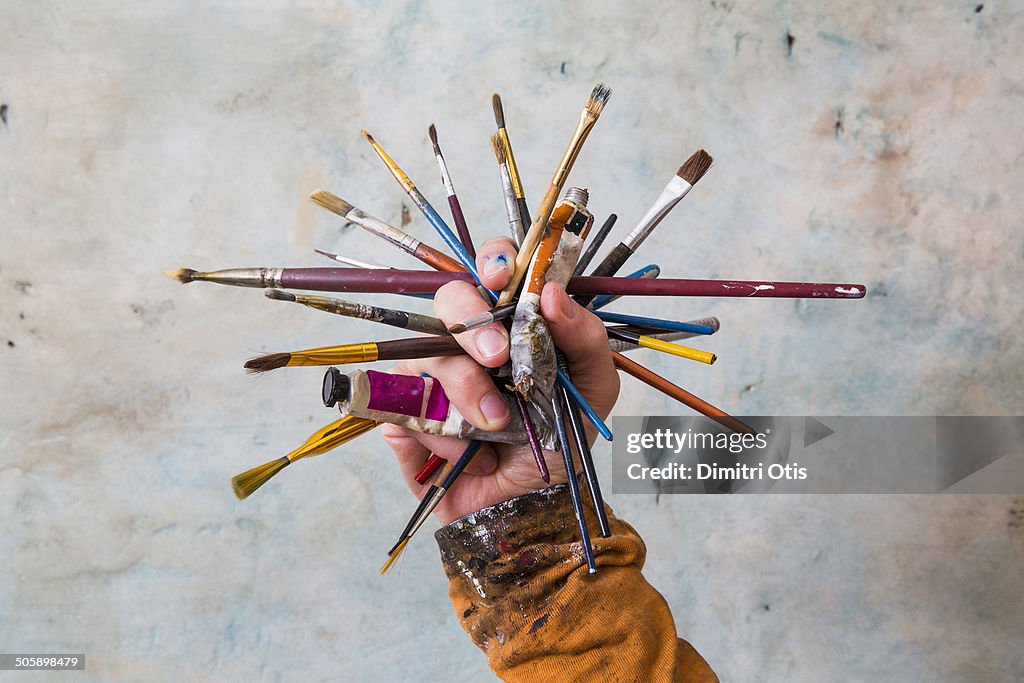 Hand holding cluster of paint brushes and paints