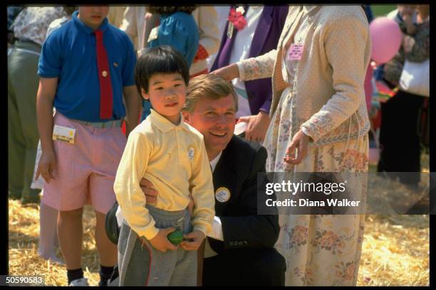 Dan Quayle , crouching, hugging little Asian-Amer. Boy, greeting children during WH Easter egg hunt.