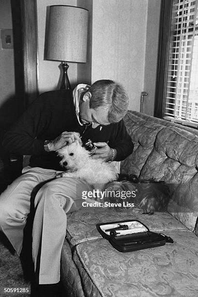 Veterinarian/Cambridge commissioner of lab animals, Stuart Wiles, sitting on couch as he uses a magnification light to examine inside ear of white...