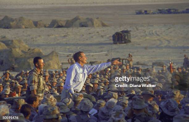 Enthused Pres. Bush tossing souvenir tie clips, perching above girding crowd of Amer. Soldiers on US-led allied gulf crisis desert duty in Saudi...