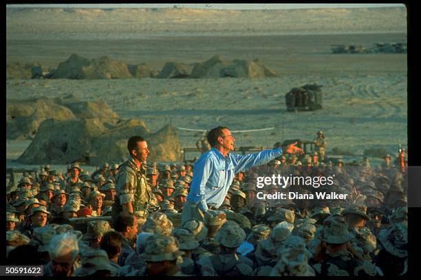 Enthused Pres. Bush tossing souvenir tie clips, perching above girding crowd of Amer. Soldiers on US-led allied gulf crisis desert duty in Saudi...