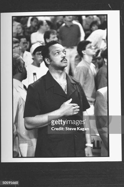 Black leader Rev. Jesse Jackson w. His hand over his heart as he stands for the National Anthem in stands at NBA basketball championship game between...