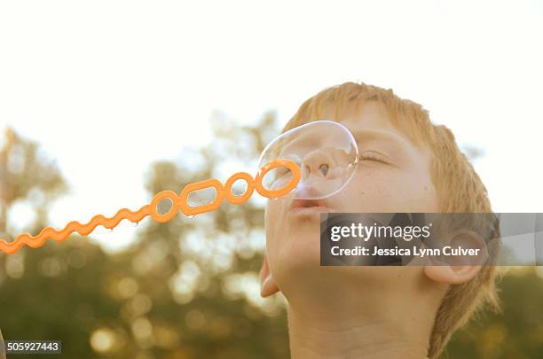 ginger haired boy blowing bubbles into the sky - ginger lynn allen stockfoto's en -beelden