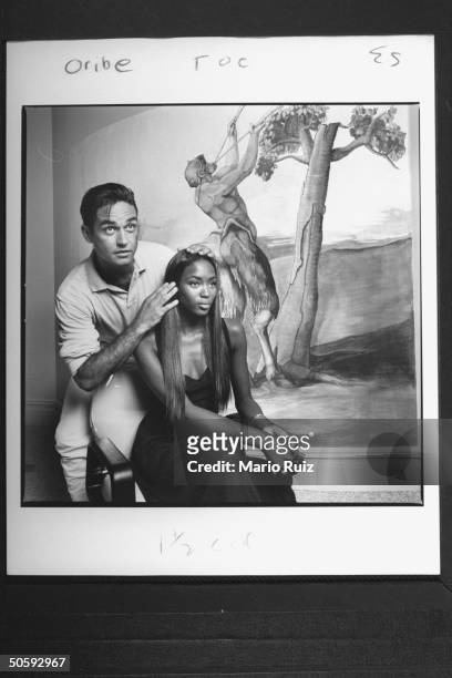 Hairdresser Oribe preparing to style the hair of model Naomi Campbell as she sits in chair next to wall mural of a satyr in salon.