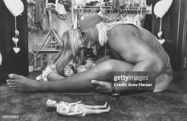 Wrestler Hulk Hogan affectionately rubbing noses w. His 3-yr-old daughter Brooke as they facing each other next to a Ken-type doll on the floor in...
