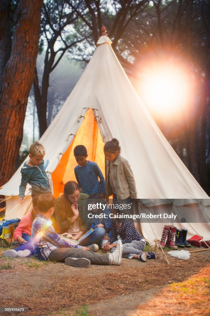 Students and teacher reading at teepee at campsite