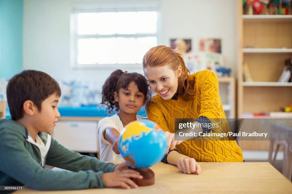 Students and teacher examining globe in classroom