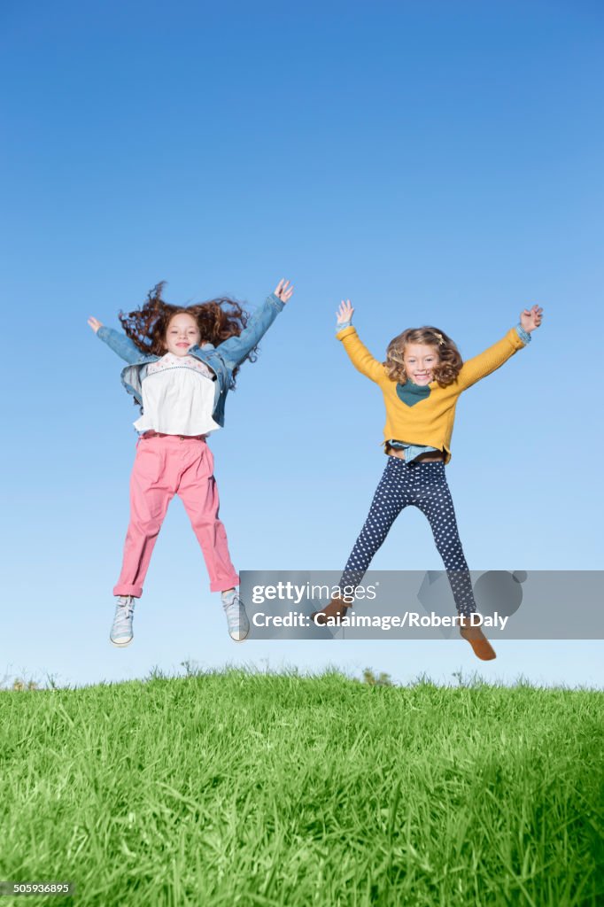 Girls jumping for joy on grassy hill