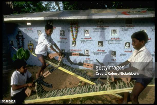 Boys on war-theme seesaws w. Bkgrd. Birth/death-dated pics of secessionist Tamil Tiger LTTE cadre battle-dead; Point Pedro, Jaffna peninsula, Sri...