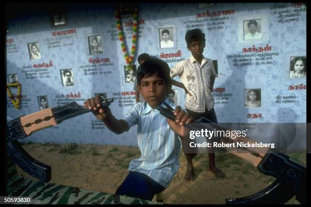 Boy on war-theme seesaw w. Wall bkgrd. Birth/death-dated pics of secessionist Tamil Tiger LTTE cadre battle-dead; Point Pedro, Jaffna peninsula.