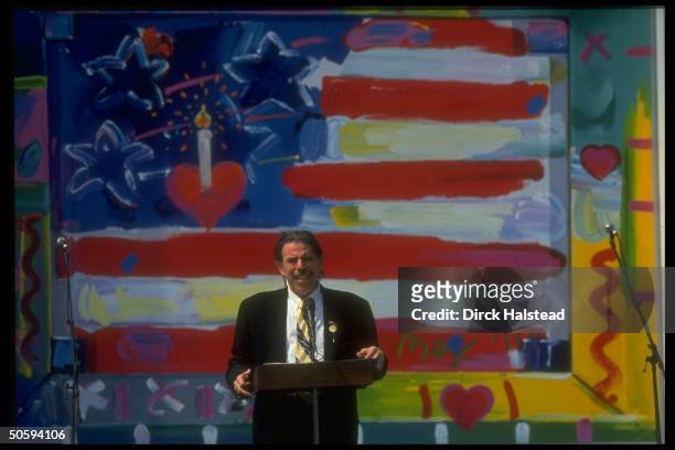 Artist Peter Max framed by his signed flag ptg., speaking at Bush WH Points of Light celebration.