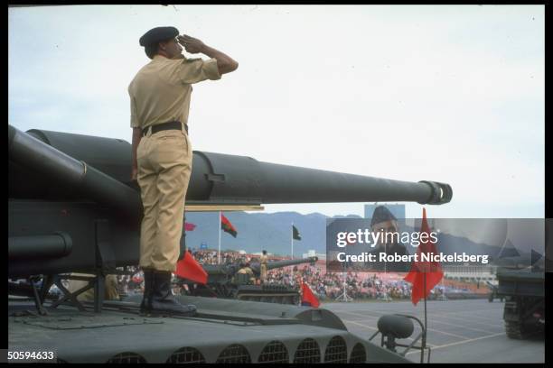 Ceremonial soldier saluting fr. His tank top perch in parade feting Pakistan Natl. Day , w. Backdrop image of founding father Mohammed Ali Jinnah.