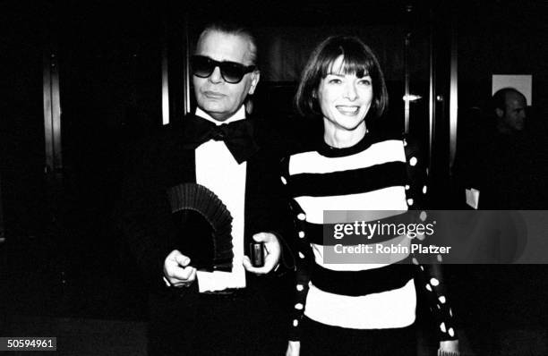 Fashion designer Karl Lagerfeld wearing tuxedo w. Large bow tie & holding hand fan, posing w. VOGUE publisher Anna Wintour at the 12th annual Council...