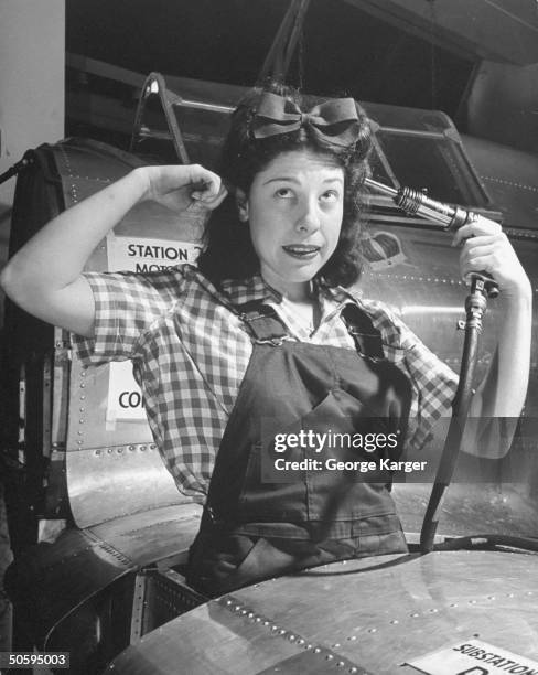 Singer Judy Canova holding drill gun to head , at wing construction station during WWII.