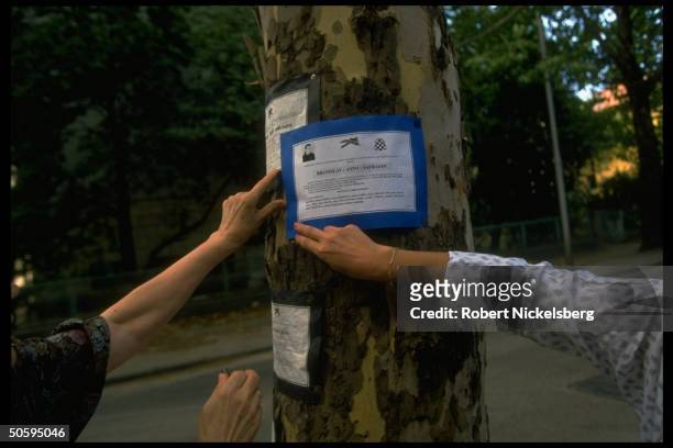 Hands affixing funeral notice to tree trunk , unknown victim in tri-ethnic civil war-torn former Yugoslav republic.