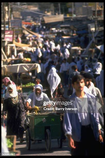 Cart-pushing Palestinian man framed by pedestrian-crammed street at Baqaa camp, world's largest, housing 1948 & 1967 Arab/Israeli war refugees.