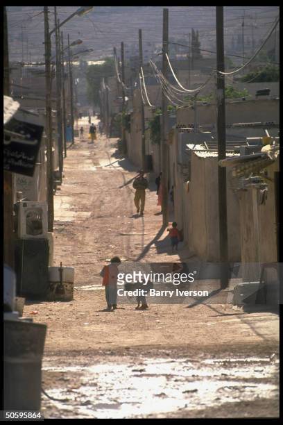 Children poised on unpaved road lined w. Crowded concrete homes at Baqaa Palestinian refugee camp, biggest in world, home to 1948 & 1967 wars...