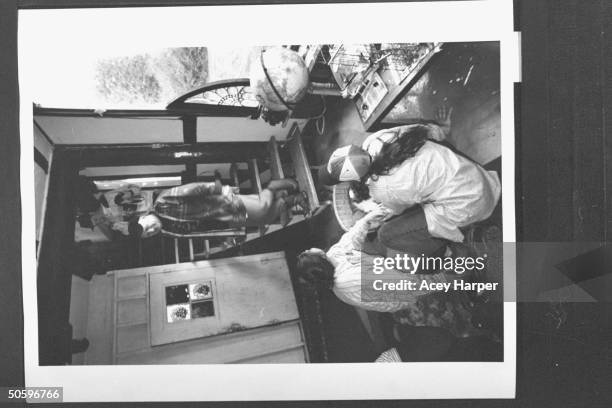 Author & '60s guru Ken Kesey standing on staircase, chatting w. Two female Hofstra Univ. Students at his home; the students are members of prof...