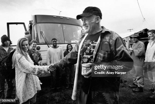 Author & '60s guru Ken Kesey shaking hands w. Hofstra Univ. Student Karen Ellick, while a group of seven other students look on nr. Their class bus...