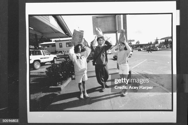 Hofstra Univ. Administrator Tamra Cimalore w. Students Daniel Elison & Stephanie Prager balancing bags of groceries on top of their head on sidewalk...