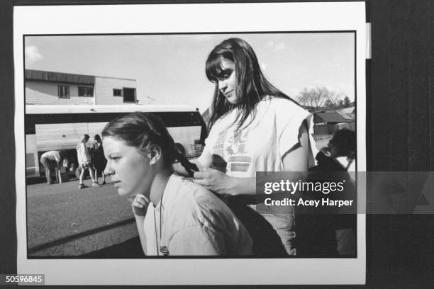 Hofstra Univ. Student Caryn Finn braiding Julie Jamilkowski's hair nr. Other students who are mulling about school bus at camping site; they are...