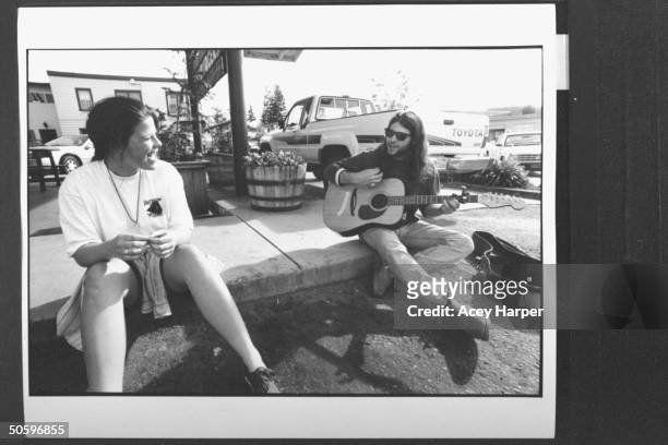 Hofstra Univ. Student Jay Caputo playing guitar & singing to Rennie Gross while sitting on sidewalk outside store; they are members of prof Douglas...