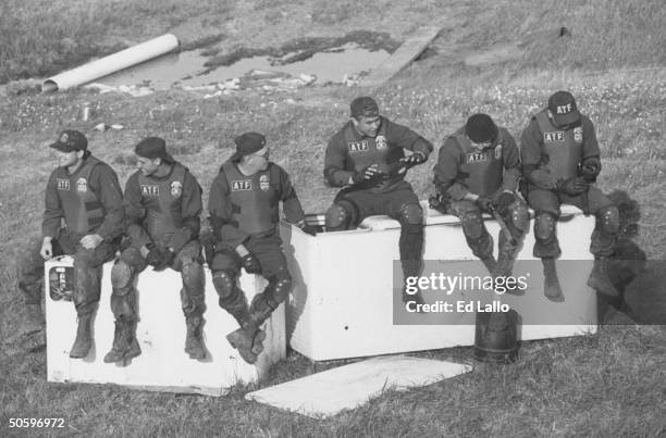 Six movie extras in combat garb as ATF agents, sitting on what look like 2 overturned refrigerators while taking a break during the filming of TV...