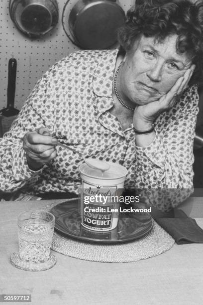 Chef Julia Child w. A very bored expression on her face as she holds a dripping spoonful of diet yogurt from a pint container of Axelrod's...