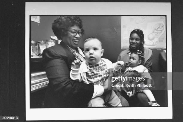 Surgeon Gen. Nominee Dr. Joycelyn Elders, the dir. Of the AR Dept. Of Public Health, holding infant boy on her lap as she sits nr. Pregnant 17-yr-old...