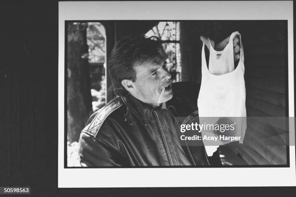Singer & Starclone perfume designer Sammy Kershaw holding up a Hanes ribbed tank top w. A cigarette in his mouth, on a recording studio's porch...