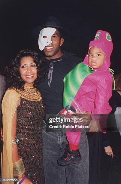 Positive, ex-basketball player Magic Johnson, wearing Phantom of the Opera mask, holding son Earvin III dressed as Barney, w. Wife Cookie clad in...