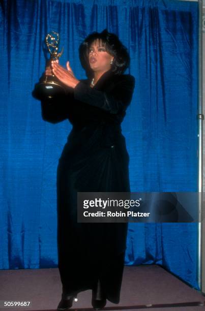 Talk show host Oprah Winfrey, wearing Thierry Mugler suit, holding aloft Emmy Award at Daytime Emmys.