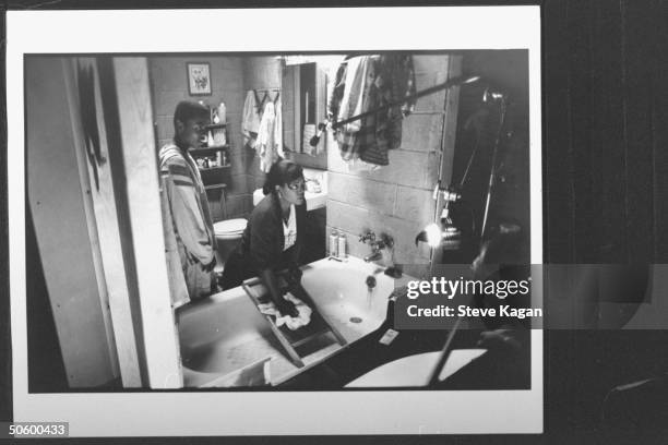 Talk show host/actress Oprah Winfrey using a washboard in bathtub as child actor Mark Lane looks on in bathroom scene on set w. Cut-away wall w. Boom...