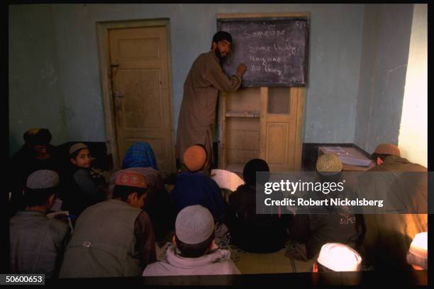 Teacher leading English language class w. All-male old & young student body at facility founded by local teachers.