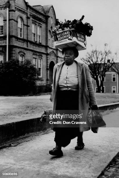 Woman carrying crate of turnip greens on her head, walking during bus boycott protesting policy of forcing African Americans to ride at the back of...