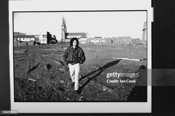 Irish folk hero Gerry Conlon, standing on muddy vacant field where Divis Flats, a famous trouble area, used to stand as church & bldgs. Loom in the...