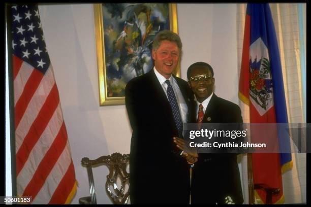 Pres. Jean-Bertrand Aristide clasping hands w. Bill Clinton, warmly greeting Pres. Attending transfer of authority from US troops to UN ceremony.